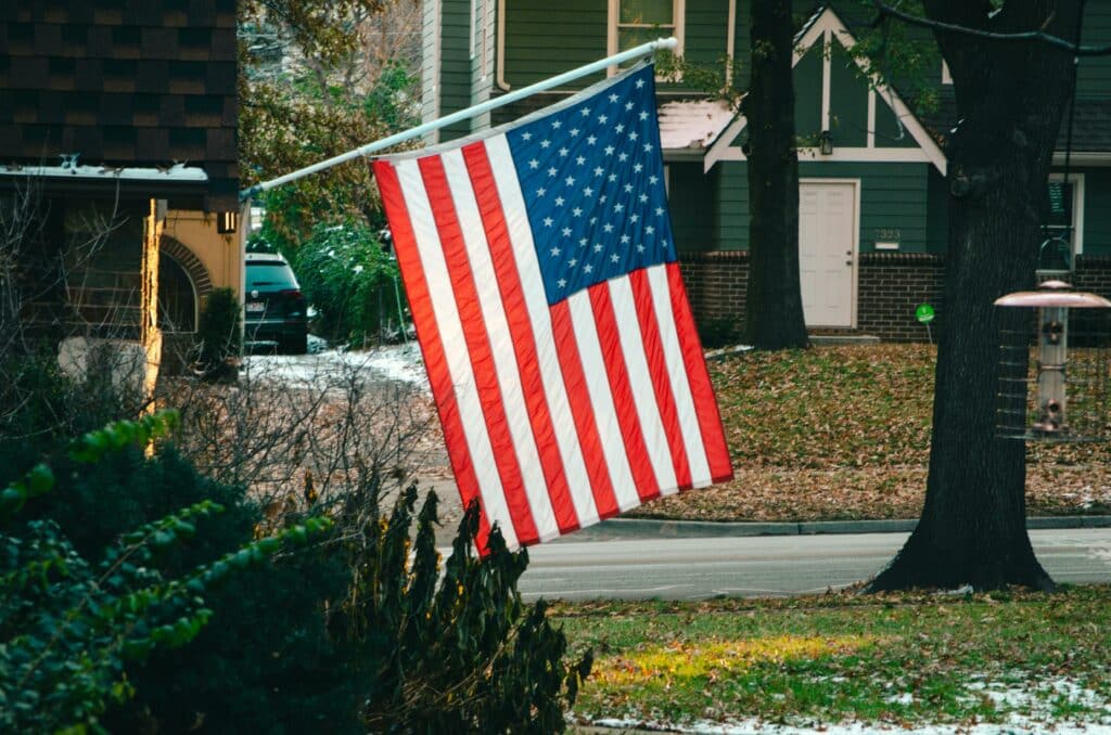 American flag flying proudly in a peaceful suburban neighborhood street.