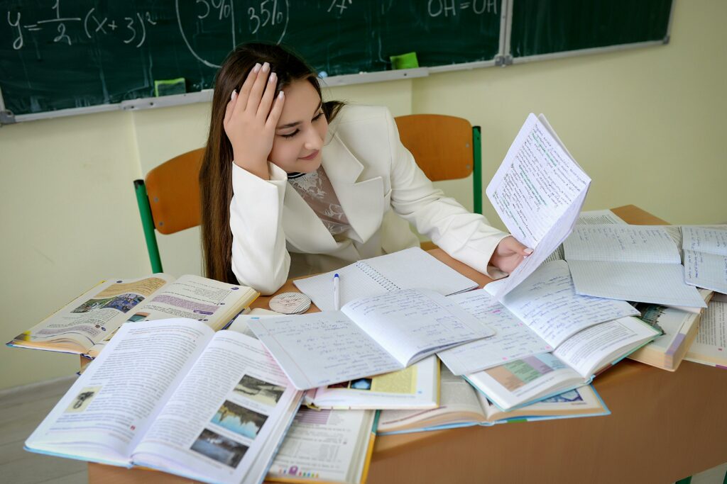 A student overwhelmed by assignments in a cluttered classroom environment.