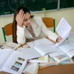 A student overwhelmed by assignments in a cluttered classroom environment.